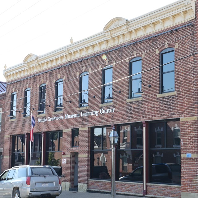 Brown brick building viewed at an angle with American flag in foreground, and large metal black sign