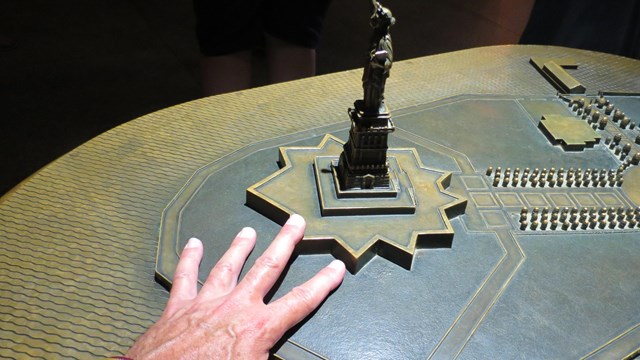 A hand touching a metal model of the Statue of Liberty.