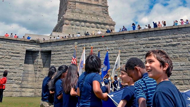 Children at the front of the Statue watch as rose petals fall from above.