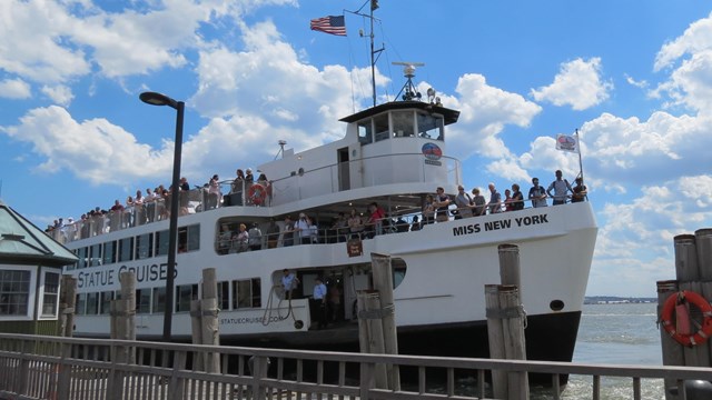 A ferry boat with passengers arrives to Liberty Island on a bright summer day.