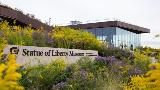 A sign reading "Statue of Liberty Museum" in a bed of flowers. 