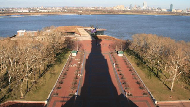 The shadow of the Statue of Liberty over brick pavement.