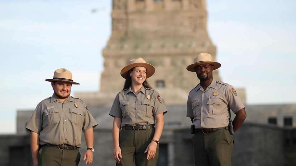 Three park rangers walking away from the back side of the Statue of Liberty