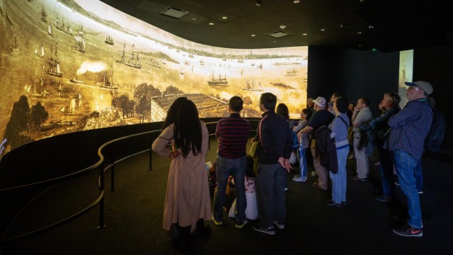 Visitors watching the informational video on the Statue of Liberty with open captions.