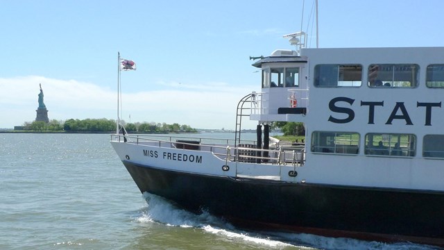 A photo of the Statue of Liberty from the distance with the ferry in the foreground..