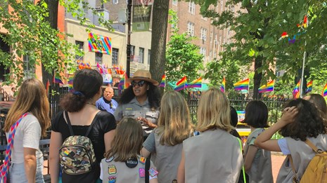 Park Ranger talking with group of young visitors inside a park surrounded by rainbow flags