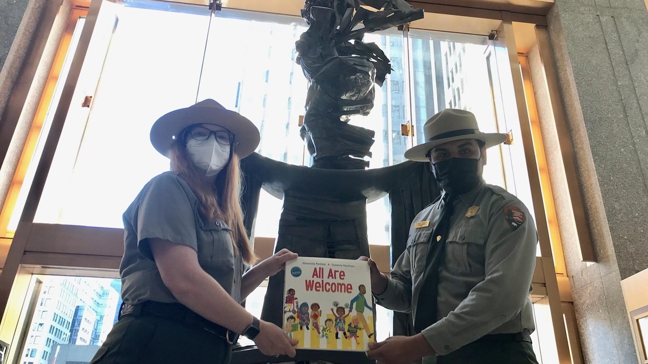Two Park Rangers displaying the book in front of a statue.