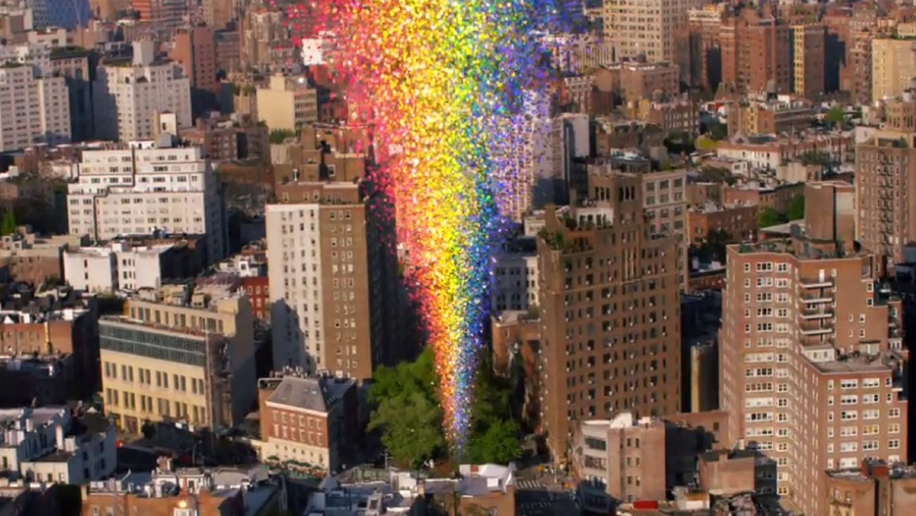 The city and a multi-colored rainbow shooting upward from a cluster of trees in the center.