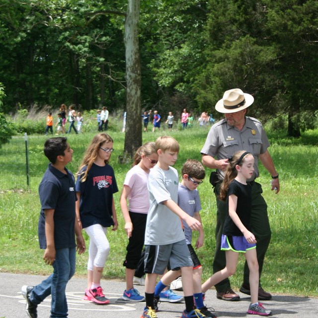 A park ranger walks alongside a group of children.