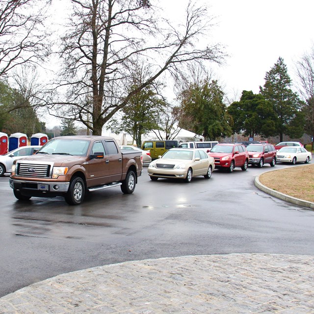 Cars line up on a road in front of the visitor center and a large white event tent.