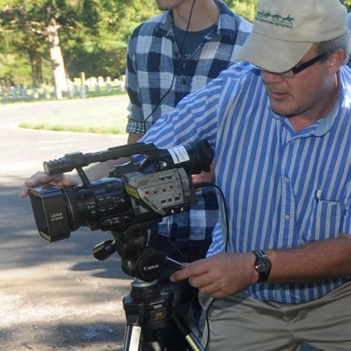 A man adjusts a video camera on a tripod.