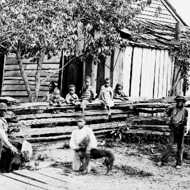 A black and white photo of African American children, some in front of a fence and some behind it.