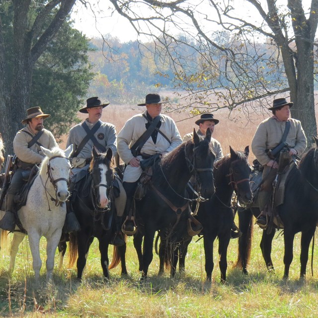A line of gray clad soldiers on horseback ride toward the viewer.