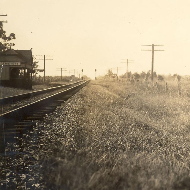 Railroad tracks pass by a platform with a sign that reads Cemetery.