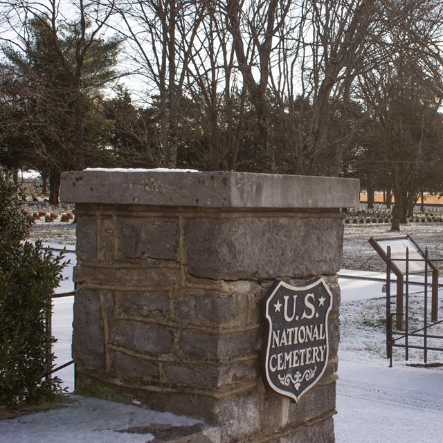 A snow-covered stone gateway with a badge shaped place that reads 