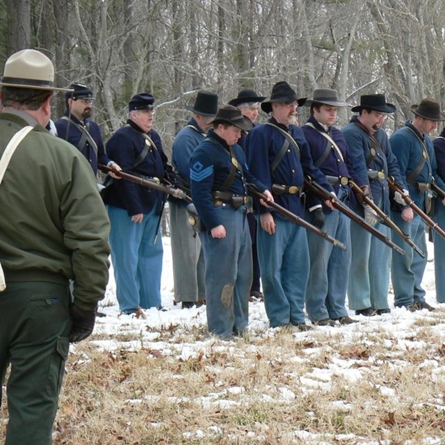 A park ranger looks on as living historians wearing Union Civil War uniforms hold muskets.