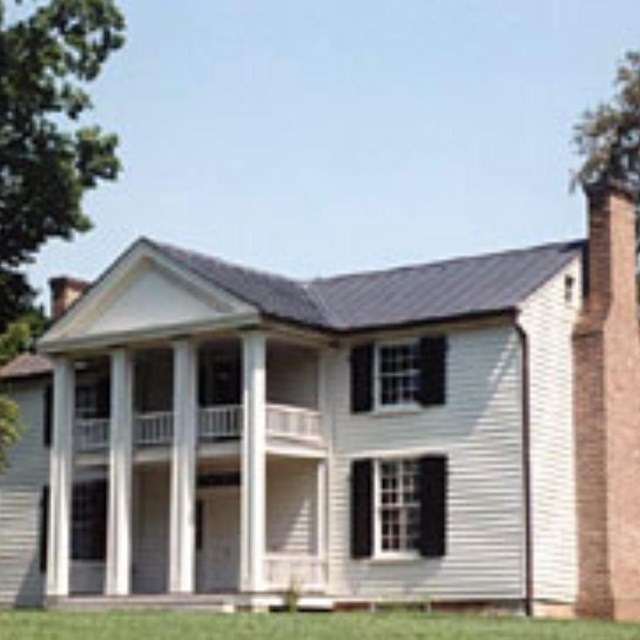 A white two story house with chimneys on each side and four square columns in front.