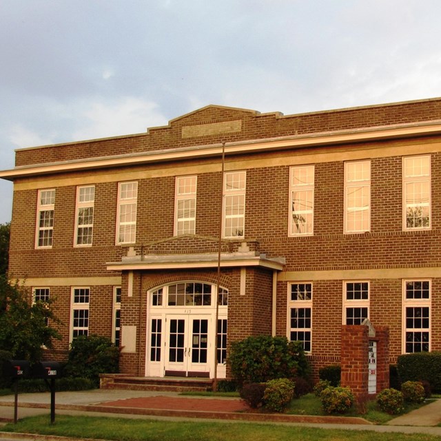 A two story brick school house with tall glass windows with the American and Tennessee state flags.