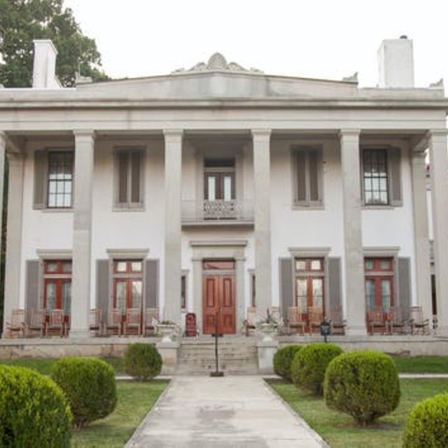 A white two story home with six columns in front of it and a walkway leading up to the door.
