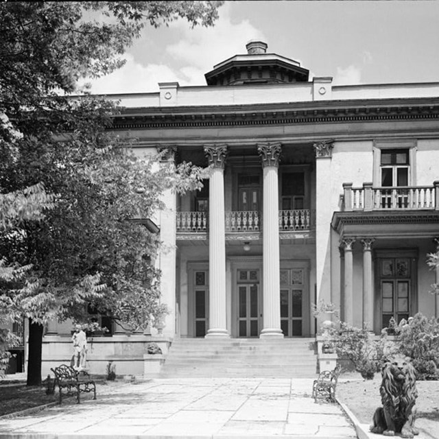 A two story home with two columns in front and a stone walkway leading to its doors.