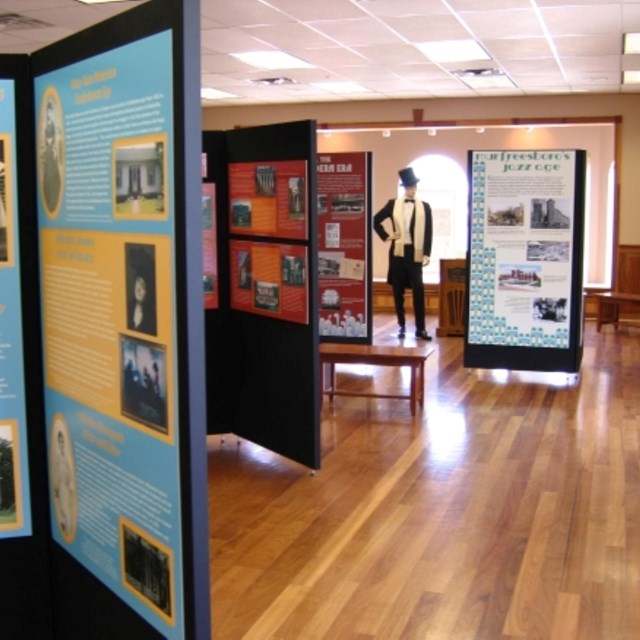 A room with museum exhibits. In the background, a mannequin is dressed in a top hat and tuxedo. 