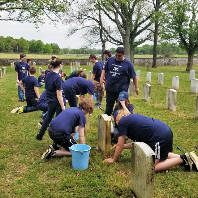 Students wearing matching t-shirts clean headstones in the Stones River National Cemetery