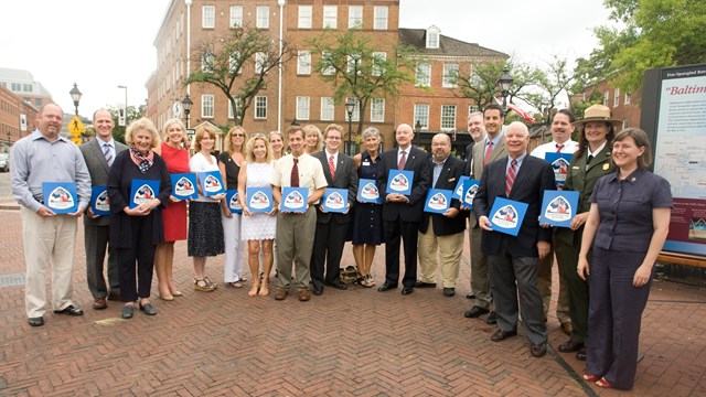 Group of people standing in next to one another in a line, each holding a small blue sign.