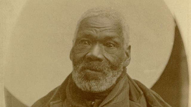 An older Black man sitting for a photo.