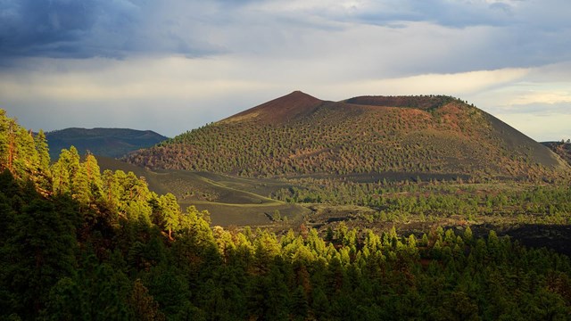 sunset crater volcano rises from a basalt lave field under a monsoon sky