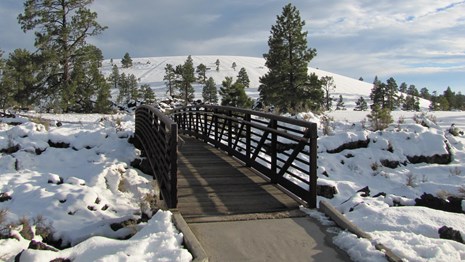A paved path with a bridge crosses a snowy, rocky landscape