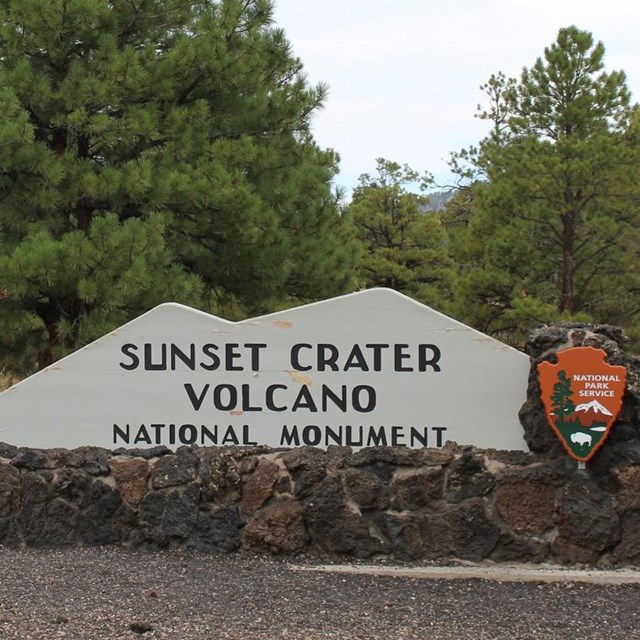 a grey, mountain-shaped sign for Sunset Crater National Monument on a roadside