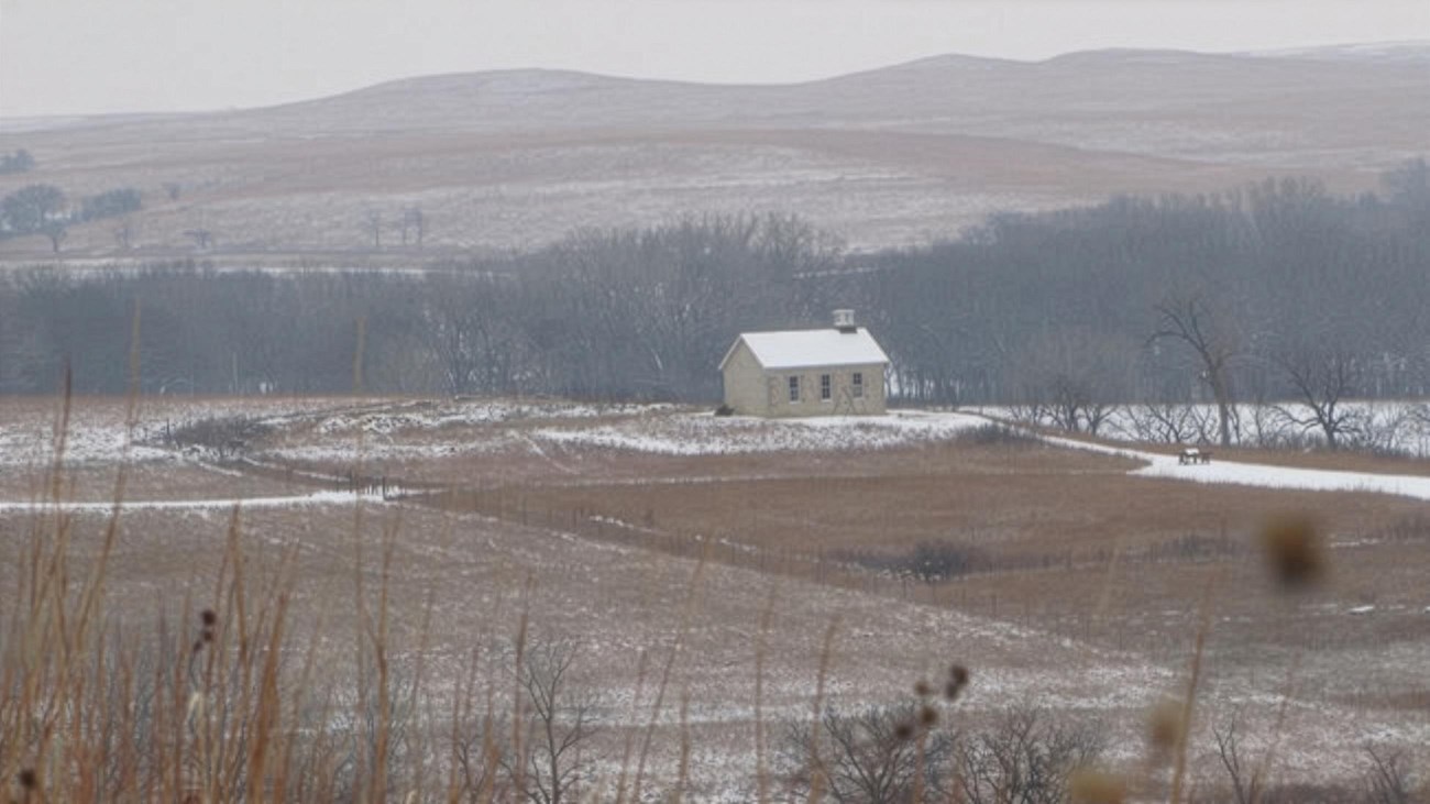 White snow covers every surface of a road leading to a stone barn.