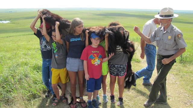 photo of kids trying on a bison hide, feeling its weight