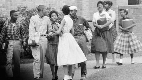 Vintage black & white photo of nine students carrying school books while laughing & talking