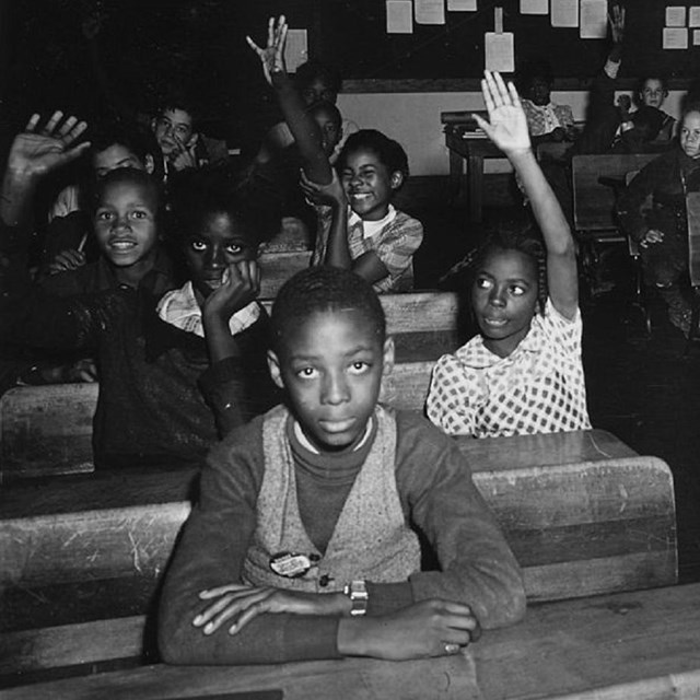 Children in classroom raising their hands. 