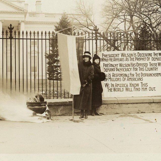 Three women protesting and party watchfires burn outside White House, Jan. 1919.