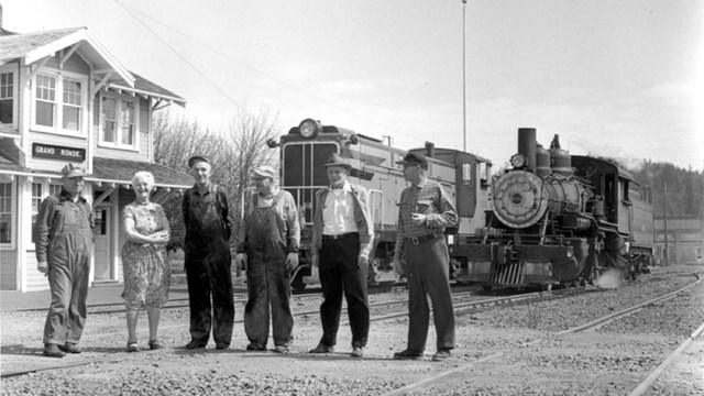 People stand in front of an old railroad track and train.
