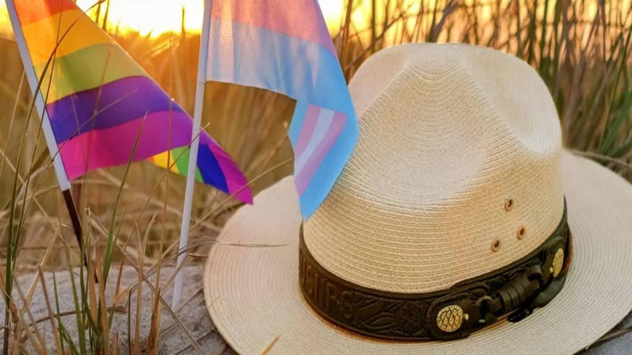 Gay pride and trans pride flag next to ranger hat on sandy dune