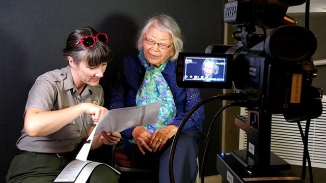 Two women look at a piece of paper in front of a camera