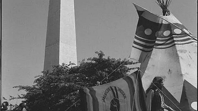 Man walks in front of tipi with Washington Monument in background.