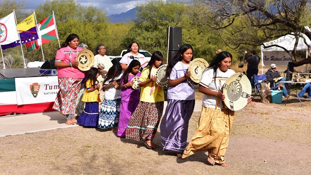 O'odham women and girls in colorful skirts holding baskets for O'odham basket dance