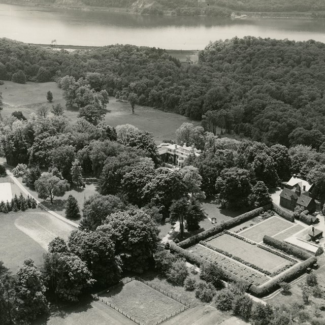 Aerial photo of a large home set among trees with a river in the background.