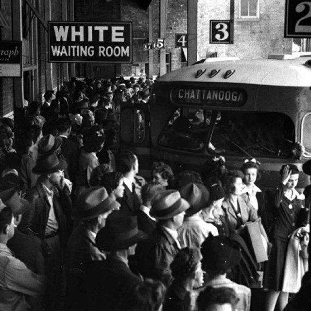 Crowd standing near a bus under sign reading White Waiting Room