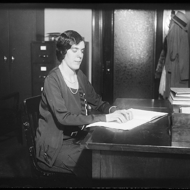 A woman reads Braille seated at a desk