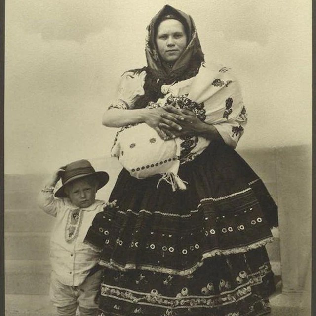 Woman in patterned skirt and headscarf stands with child