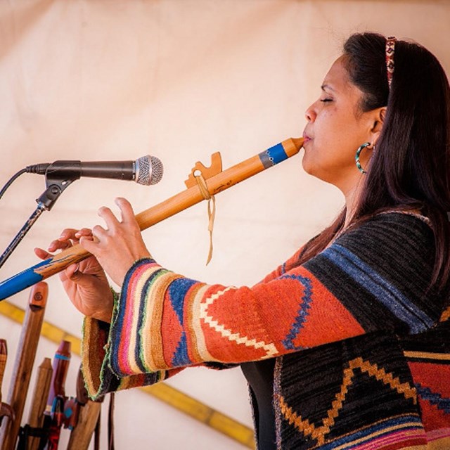 Woman wearing colorful clothing plays a wind instrument into a microphone