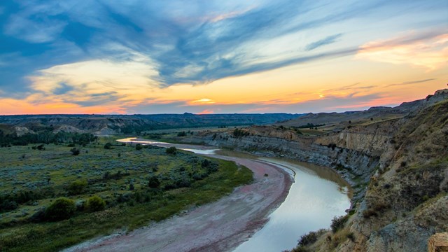 A river winds through badlands landscape with a blue and orange hued sky.