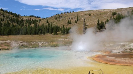 Steam rises from a blue-, yellow- and orange-colored hot spring.