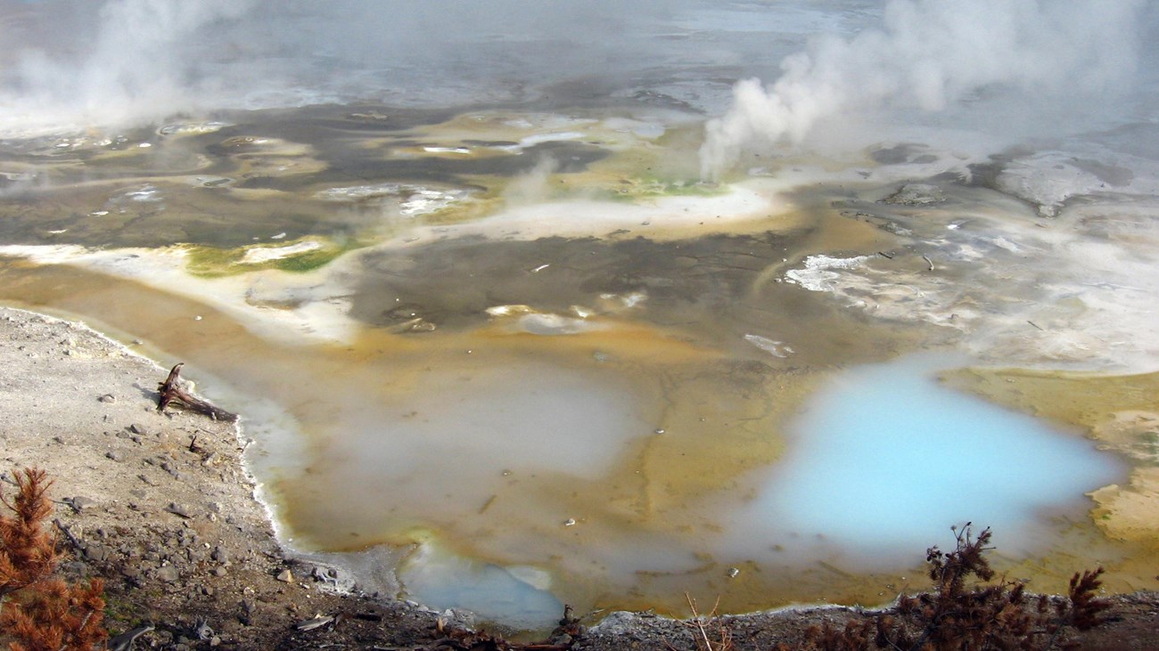 Multicolored ground dotted with milky blue pools of hot water and rising steam.