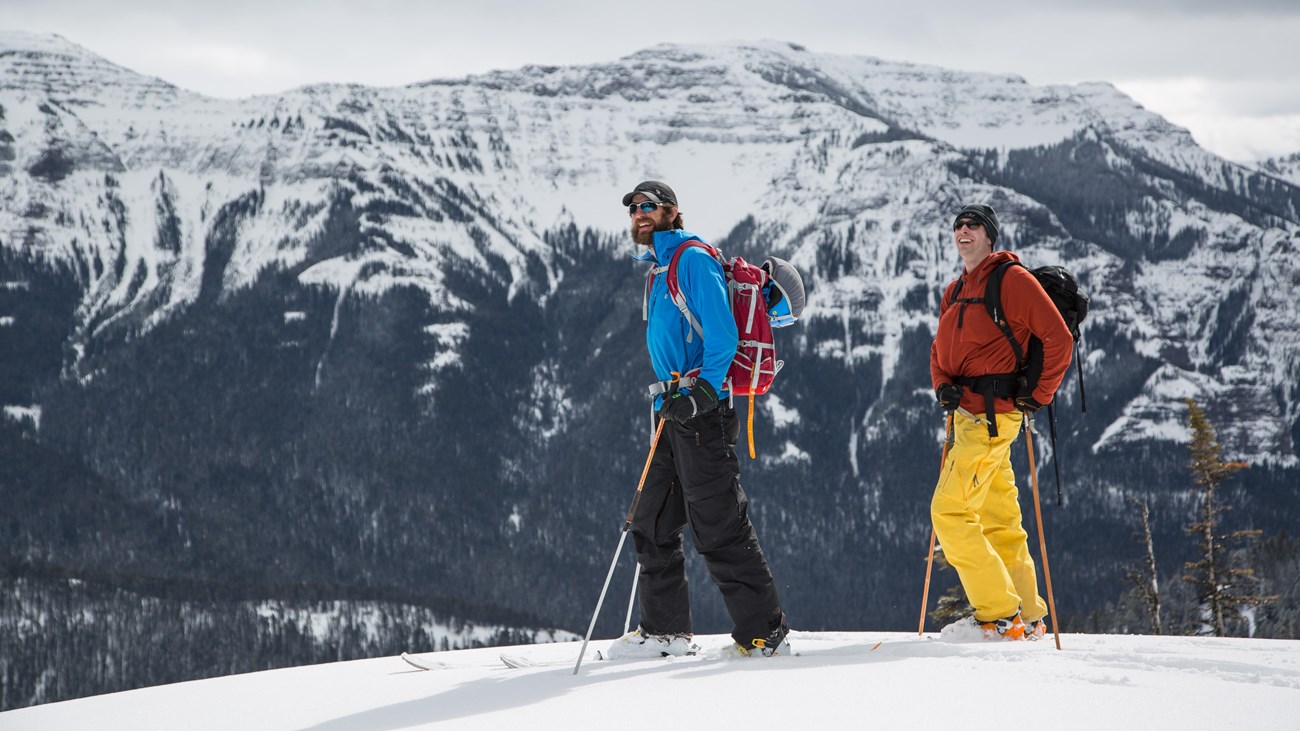 Two backcountry skiers look onward with mountain views in the background.